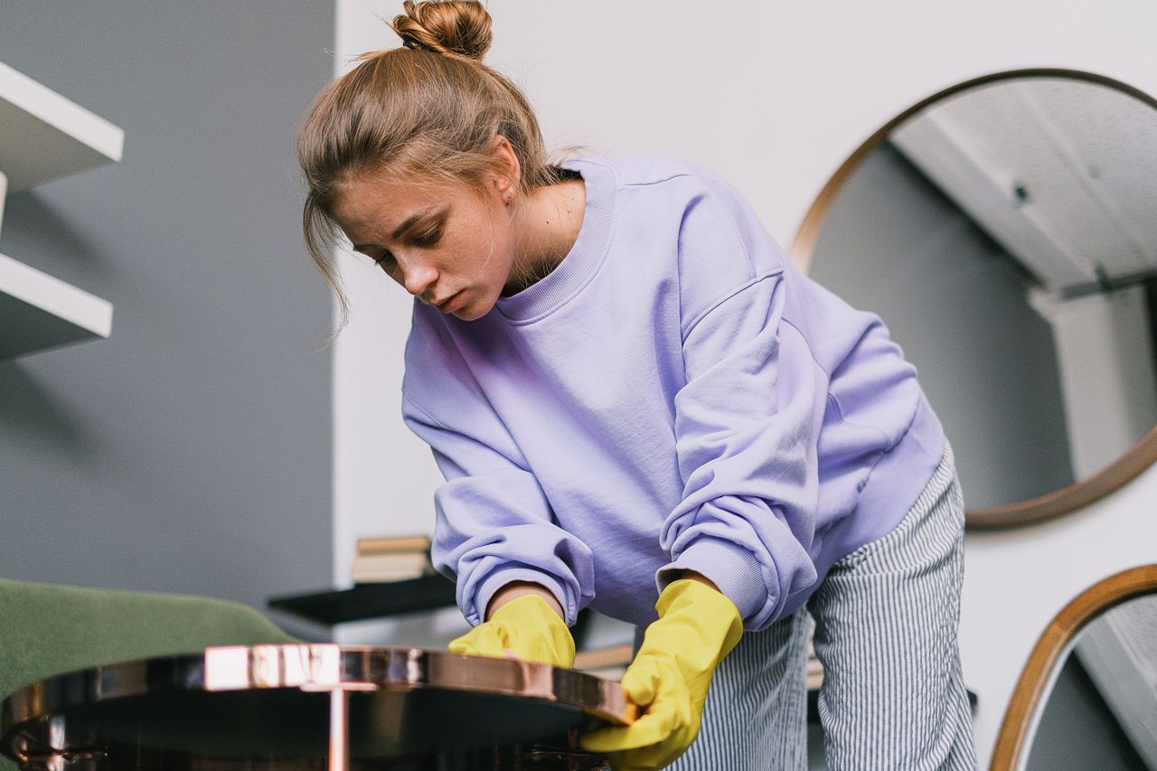 services-01 From below of young female in casual clothes and latex gloves standing and wiping table against mirrors in light room in daytime