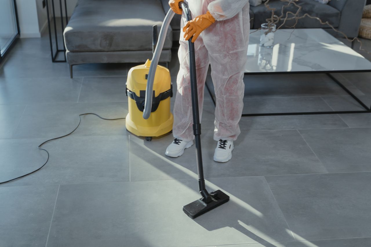 services-02 A professional cleaner in protective gear vacuuming the floor in a modern living room.