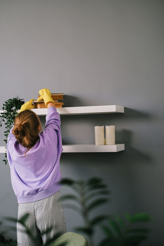 why-choose-us Back view of unrecognizable female in casual clothes and latex gloves standing and taking books while cleaning shelves in room with gray wall
